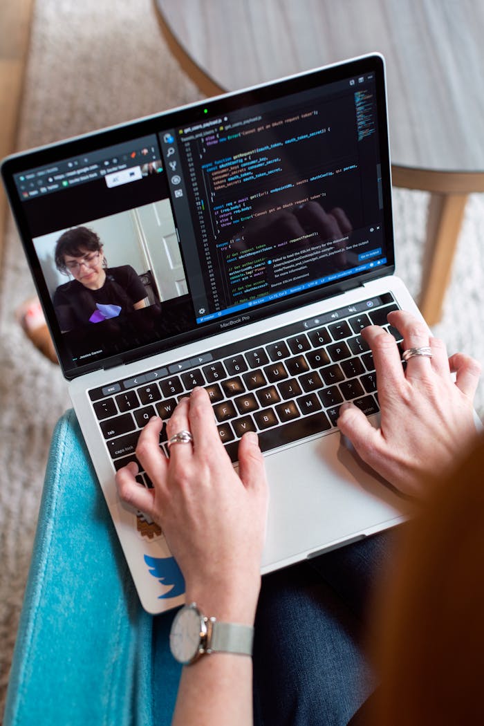 Person coding on a laptop during a video conference, showcasing remote work.