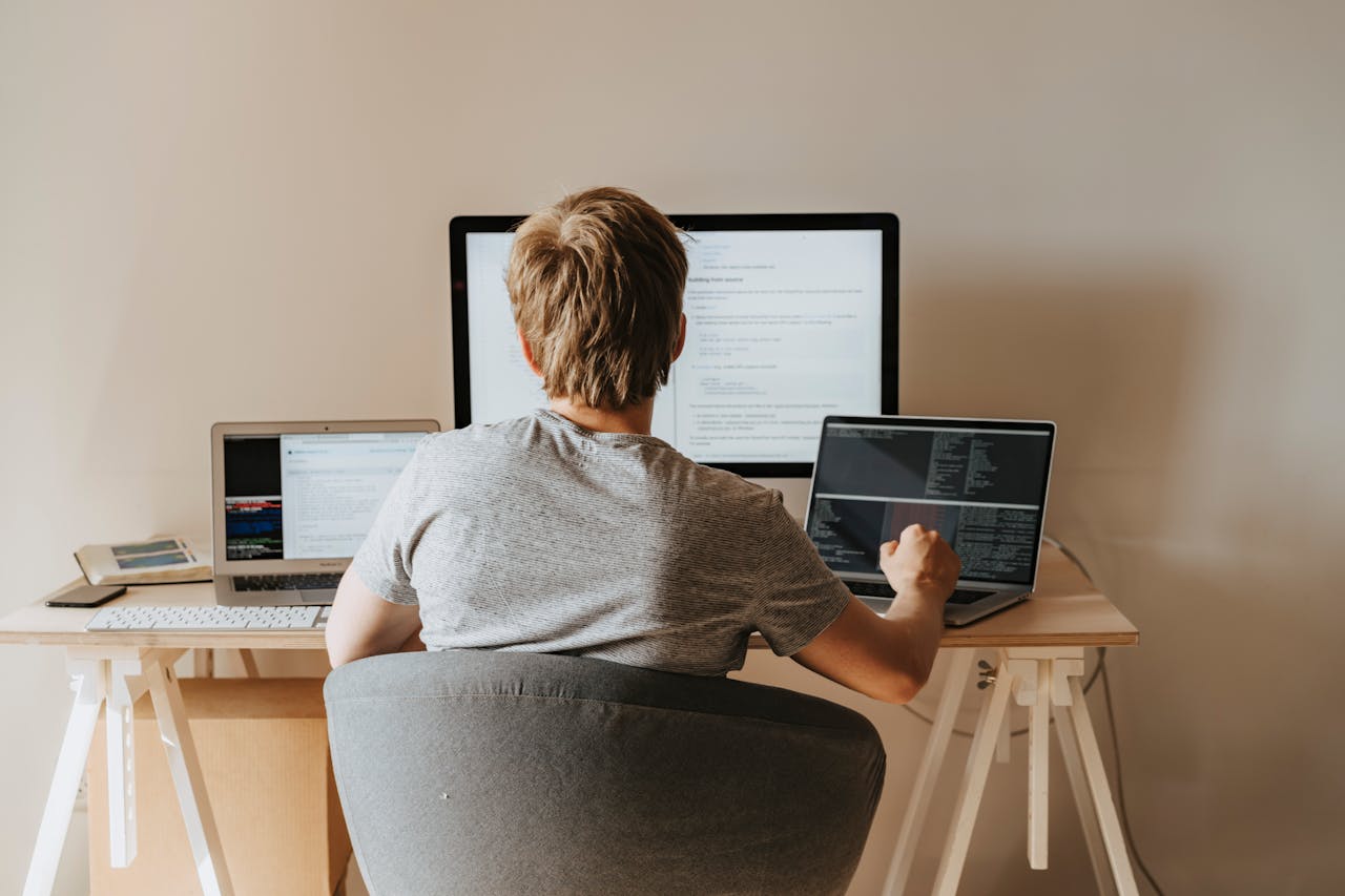 Teen programming with multiple laptops in a modern workspace. Ideal for tech and education themes.